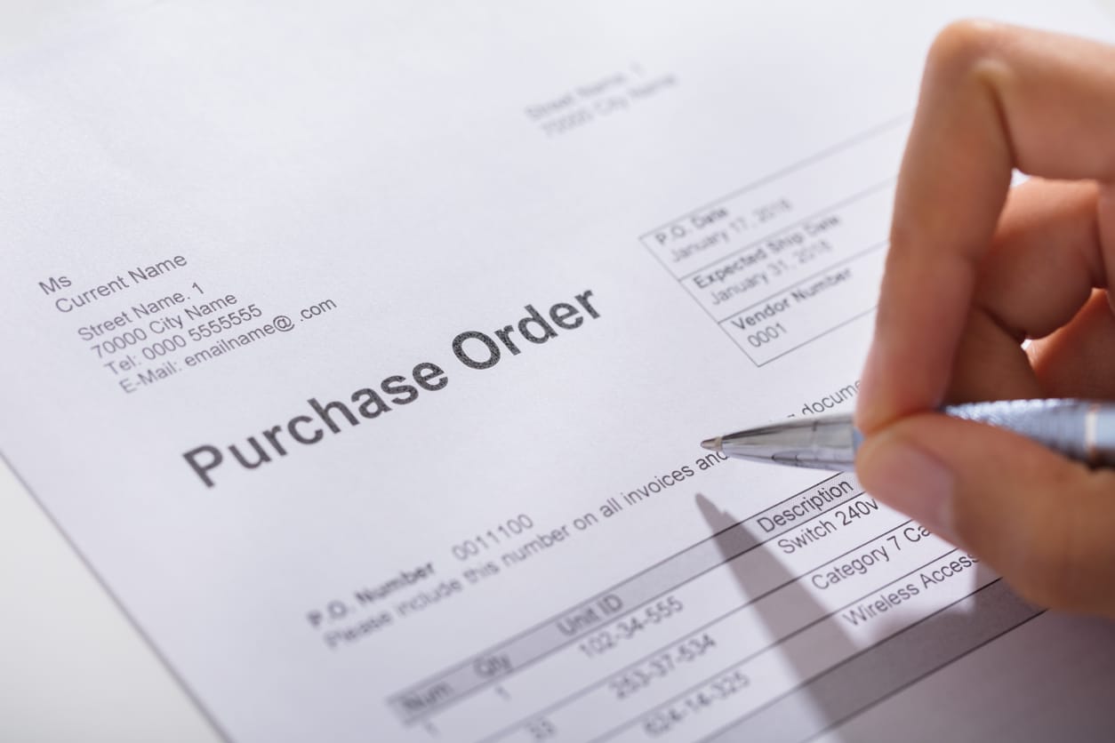 Close-up Of A Person Hand Filling A Purchase Order Form On Wooden Desk