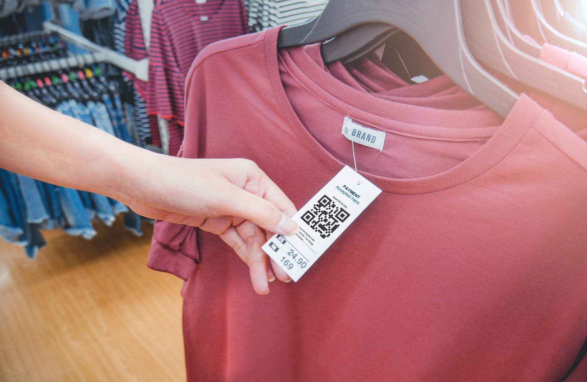 Woman's hand with a cloth hang tags label with QR code price tag in a clothing shop.