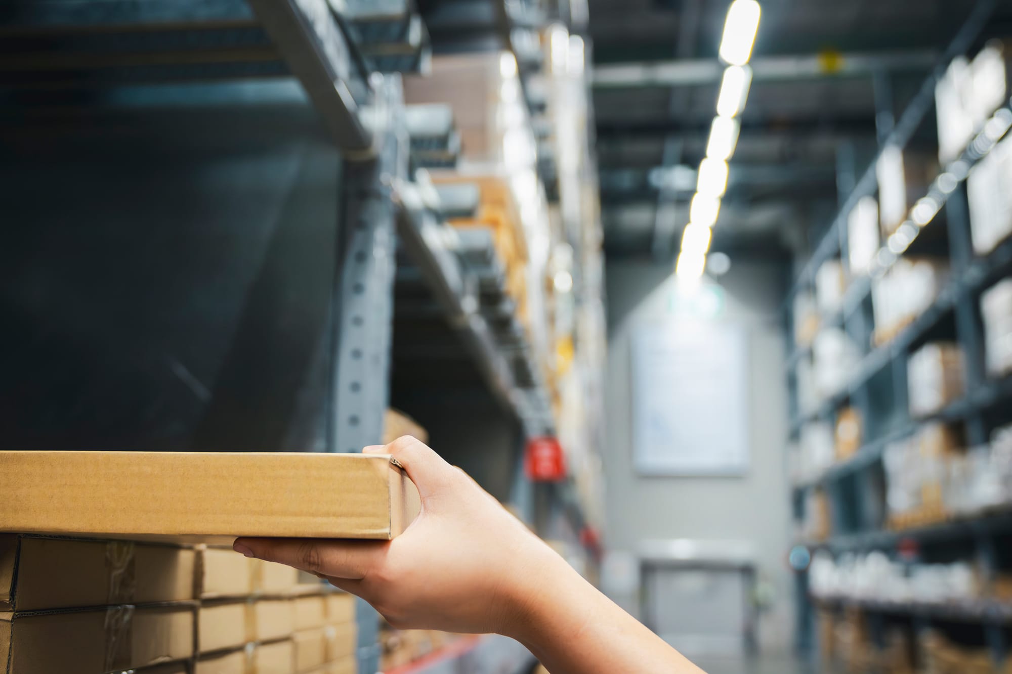 Close-up of a worker’s hand picking a cardboard box from a warehouse shelf