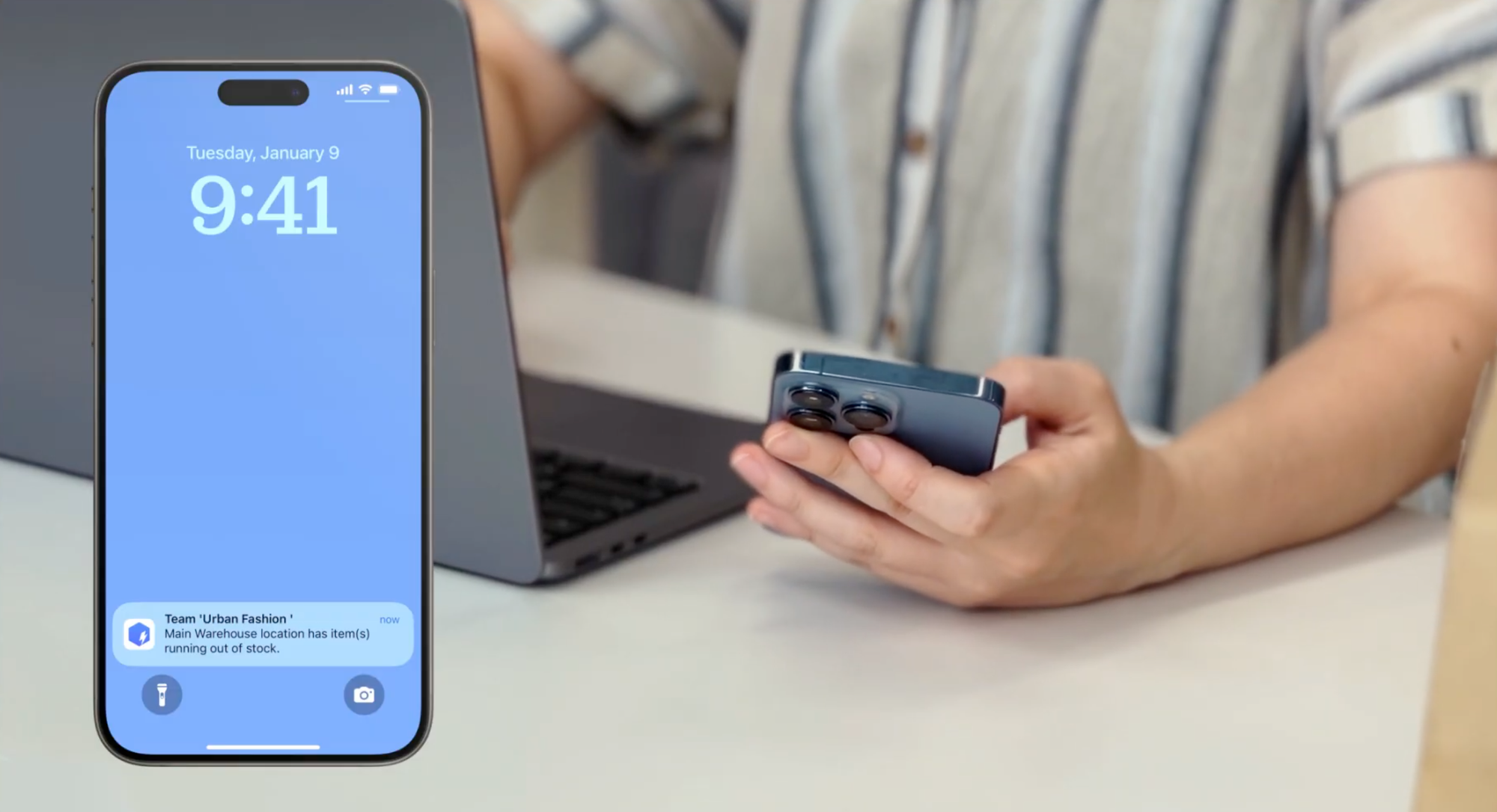 A person holding a smartphone with a BoxHero app push notification for low stock alert