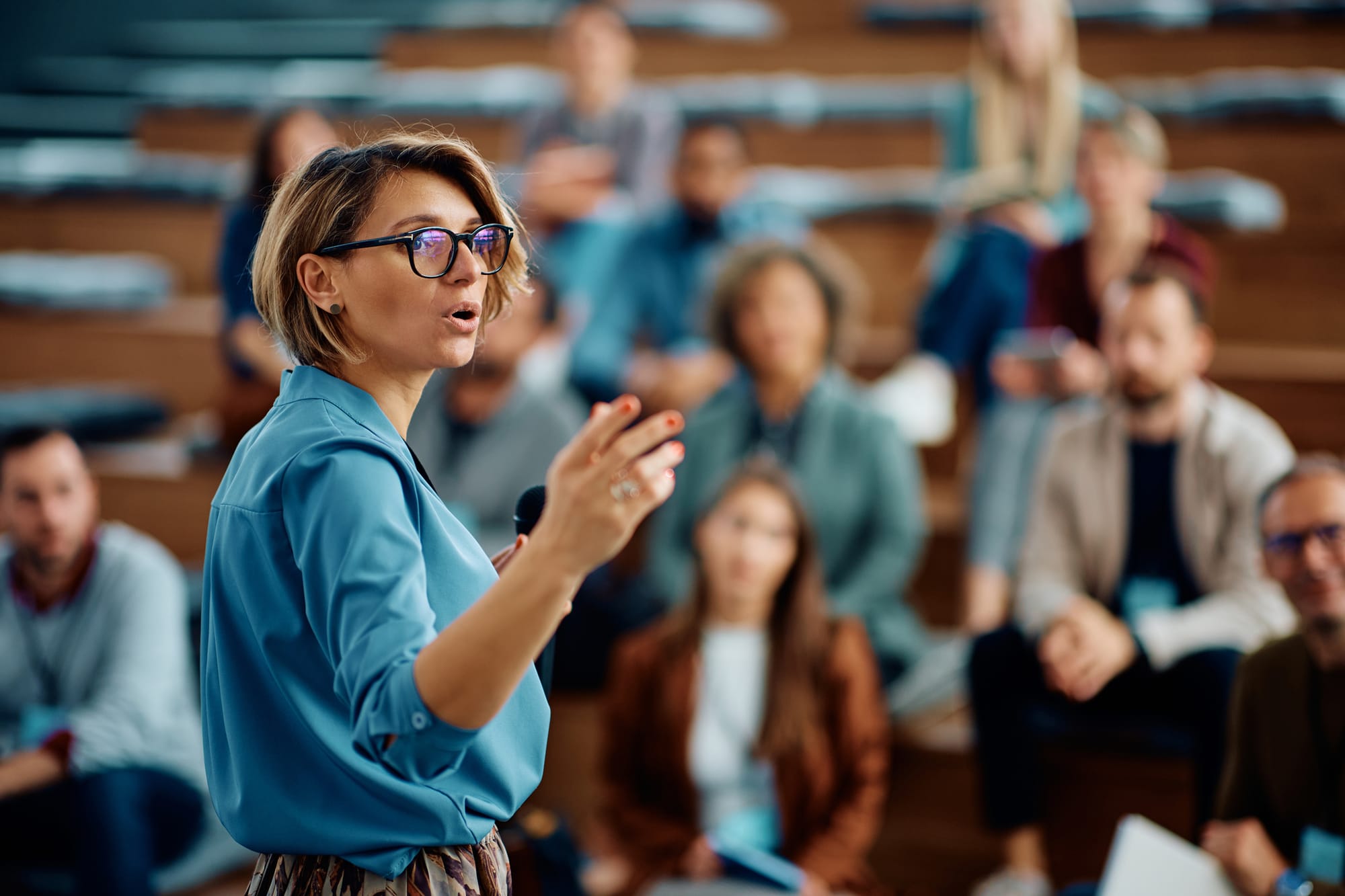 A businesswoman talking to group of seminar attendees and/or staff members in a conference hall.