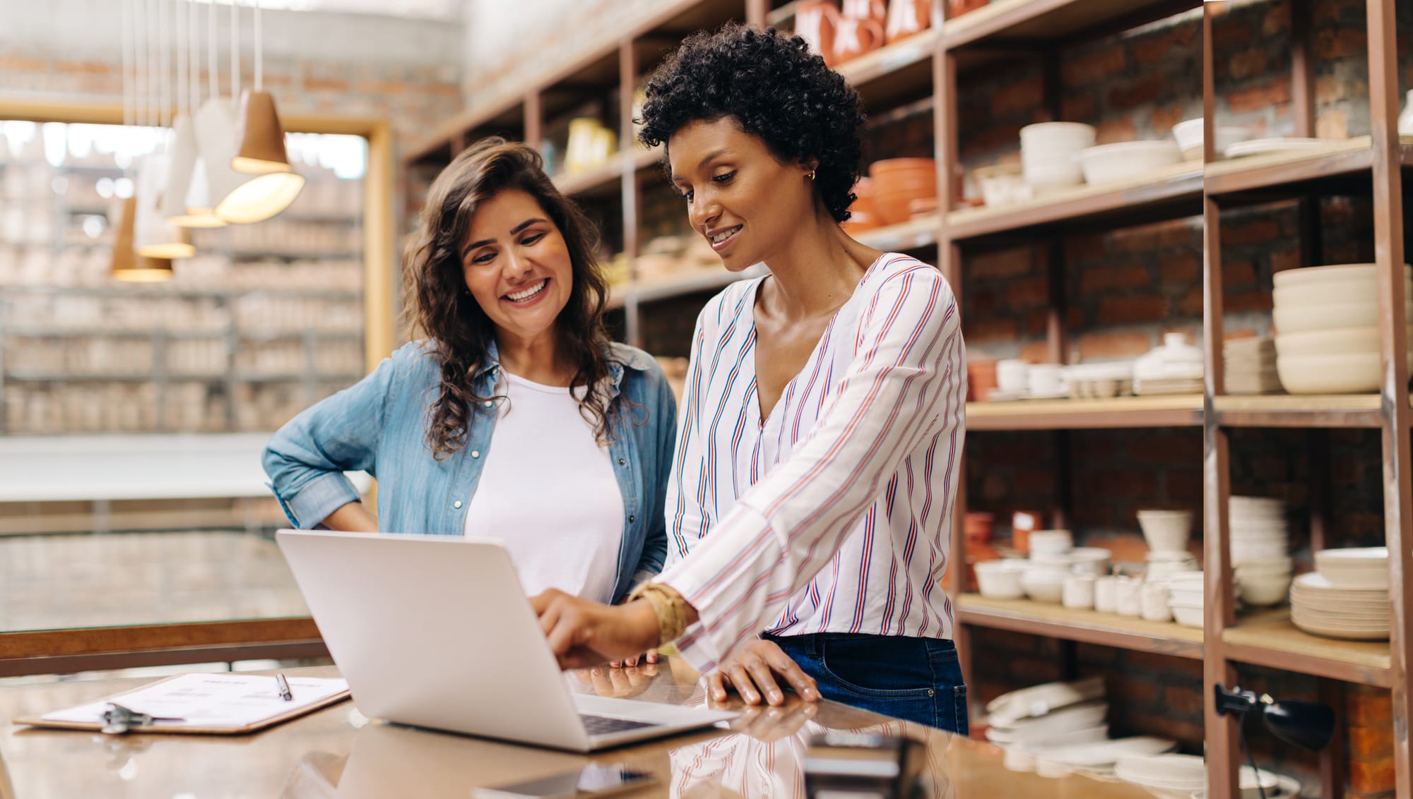 Two female entrepreneurs managing online orders in their store using a laptop.