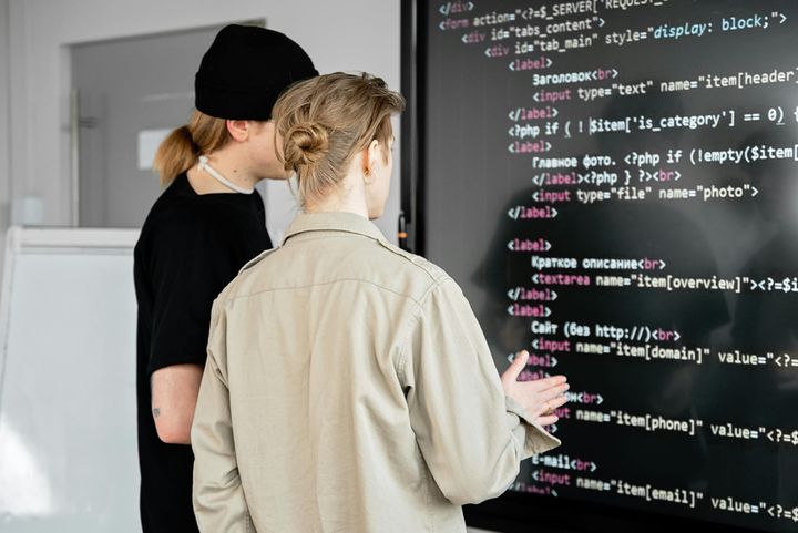 Two people discussing code displayed on a large screen in a tech setting.