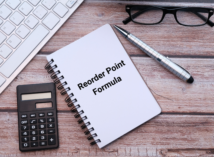 Office desk with spiral notebook, pen, calculator, keyboard, and glasses