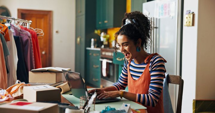 Small business owner managing inventory from home, surrounded by packages and clothing in a kitchen workspace.