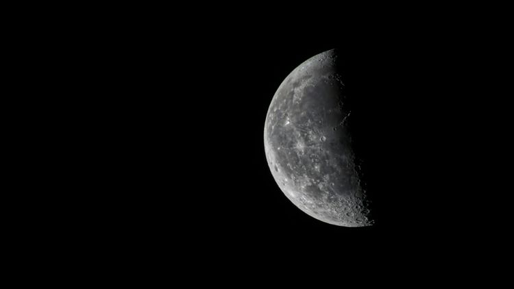 A view of the Moon, illuminated on the left and dark on the right, against the dark night.