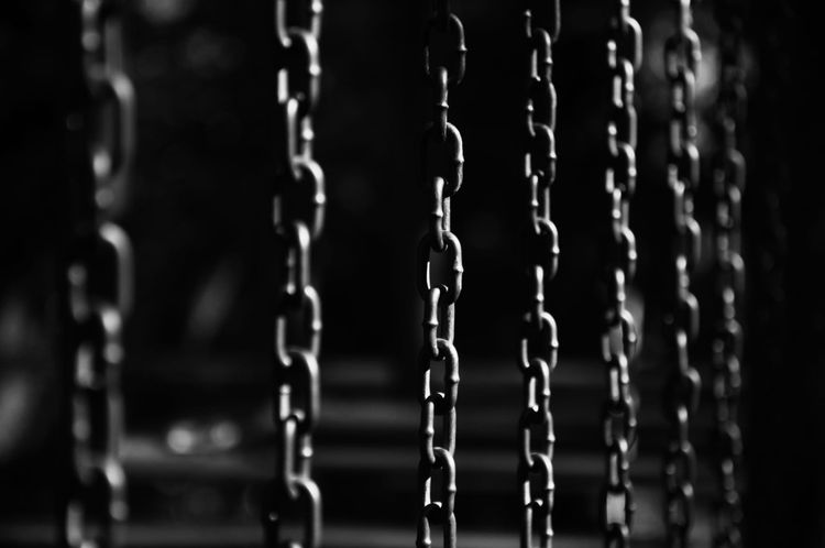 A black and white photo of several hanging chains against a dark background.