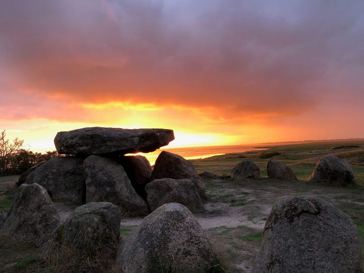 A collection of boulders covered by a flatter stone slab, surrounded by other stones in a circle. It's either sunrise or sunset.