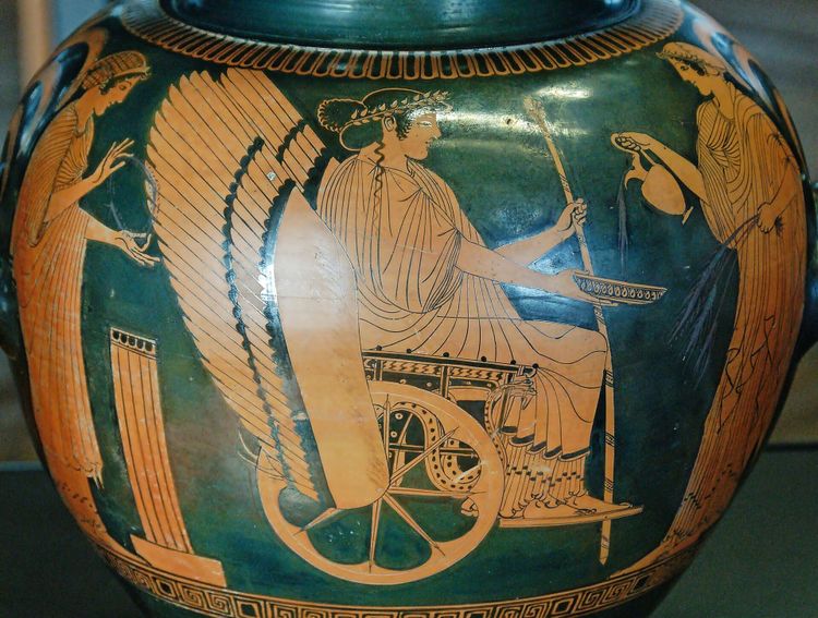 Ancient Greek pottery in the red-figure style. A goddess in the center sits in a winged chariot, accompanied by other figures who serve her.