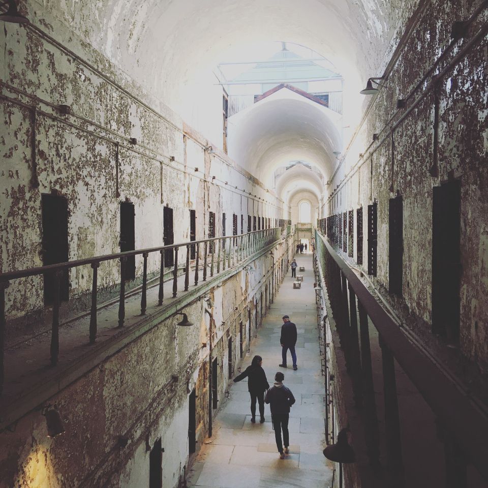 A two-storey prison cell block. It's in disrepair and clearly isn't used anymore. A few people are walking around it.