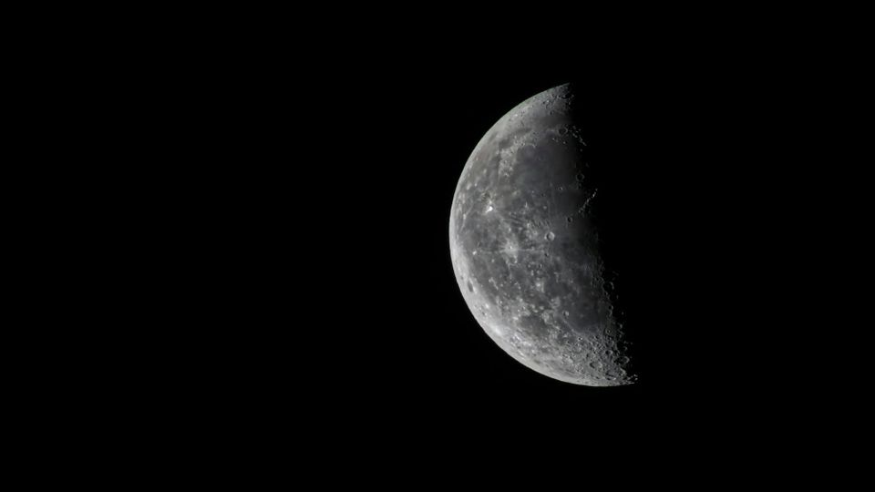 A view of the Moon, illuminated on the left and dark on the right, against the dark night.
