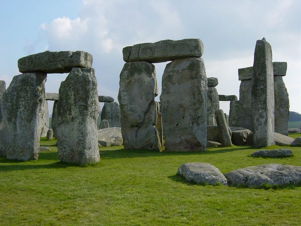 A view of several megalithic structures that form part of Stonehenge, with green grass and cloudy skies.