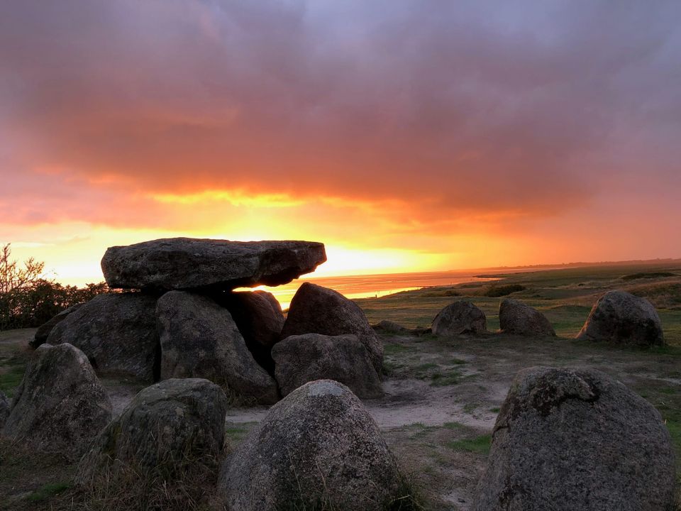 A collection of boulders covered by a flatter stone slab, surrounded by other stones in a circle. It's either sunrise or sunset.