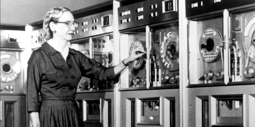 Grace Hopper, who originated the convention of calling errors in code "bugs", looks at some old-fashioned tape machines. 
