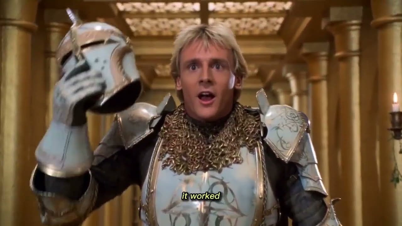 A blond knight in white-and-gold armor holds up his helmet in a golden hall, subtitled &ldquo;it worked&rdquo;