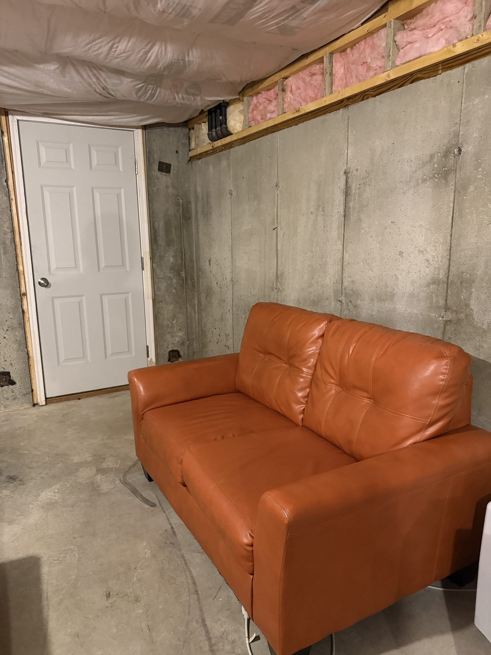 The real thing: the orange loveseat from Facebook Marketplace, the white bulkhead door, and the pink insulation along the rim joist