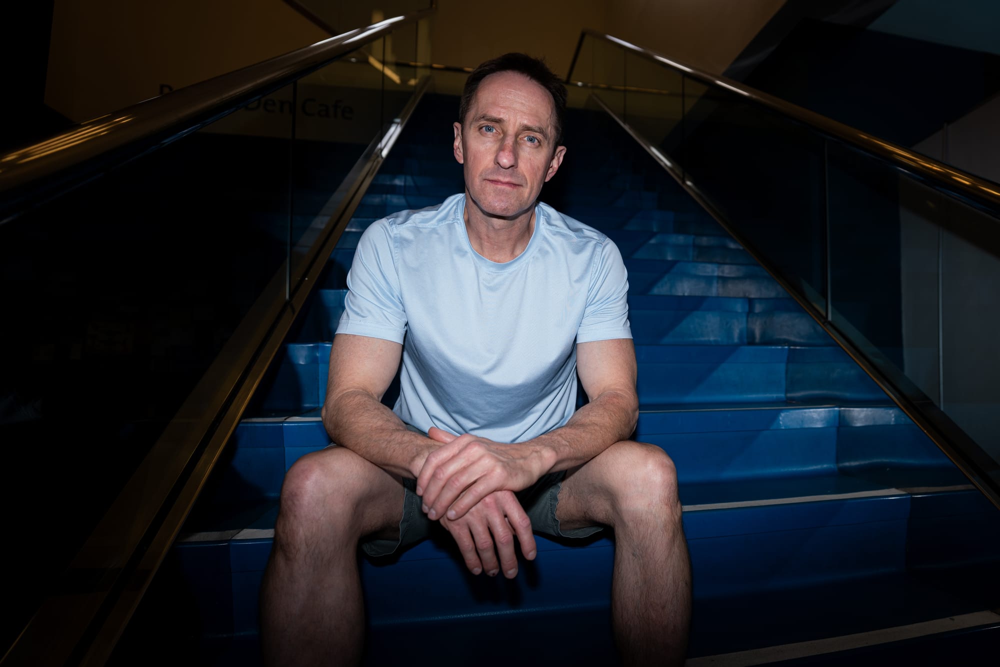 Ron Blake person sits on blue stairs, wearing a light blue shirt and shorts.