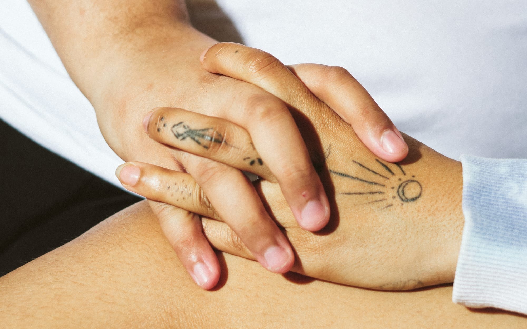 Two hands with tattoos are gently holding each other.