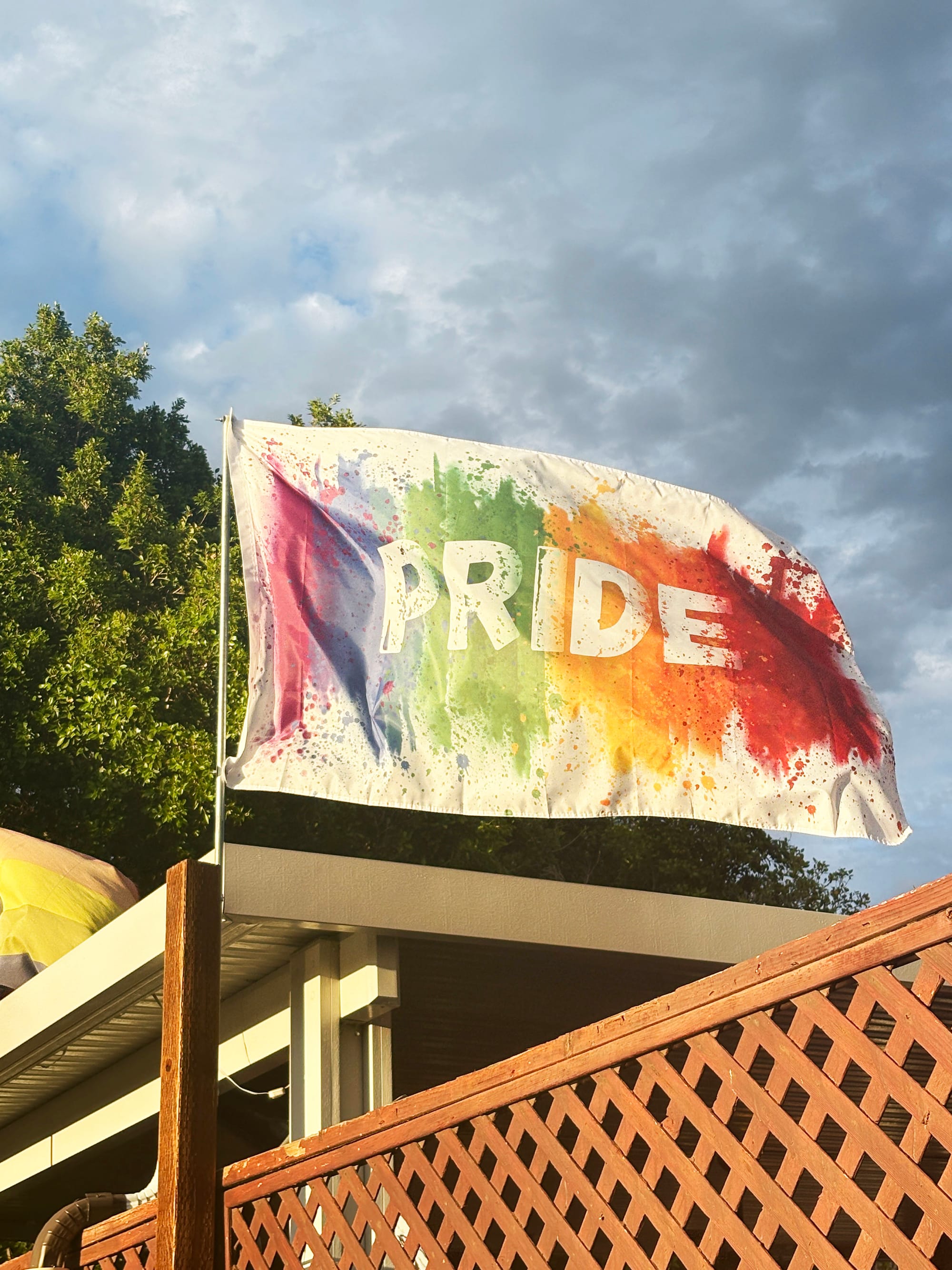 A colorful pride flag with the word "PRIDE" on it, set against a partly cloudy sky.