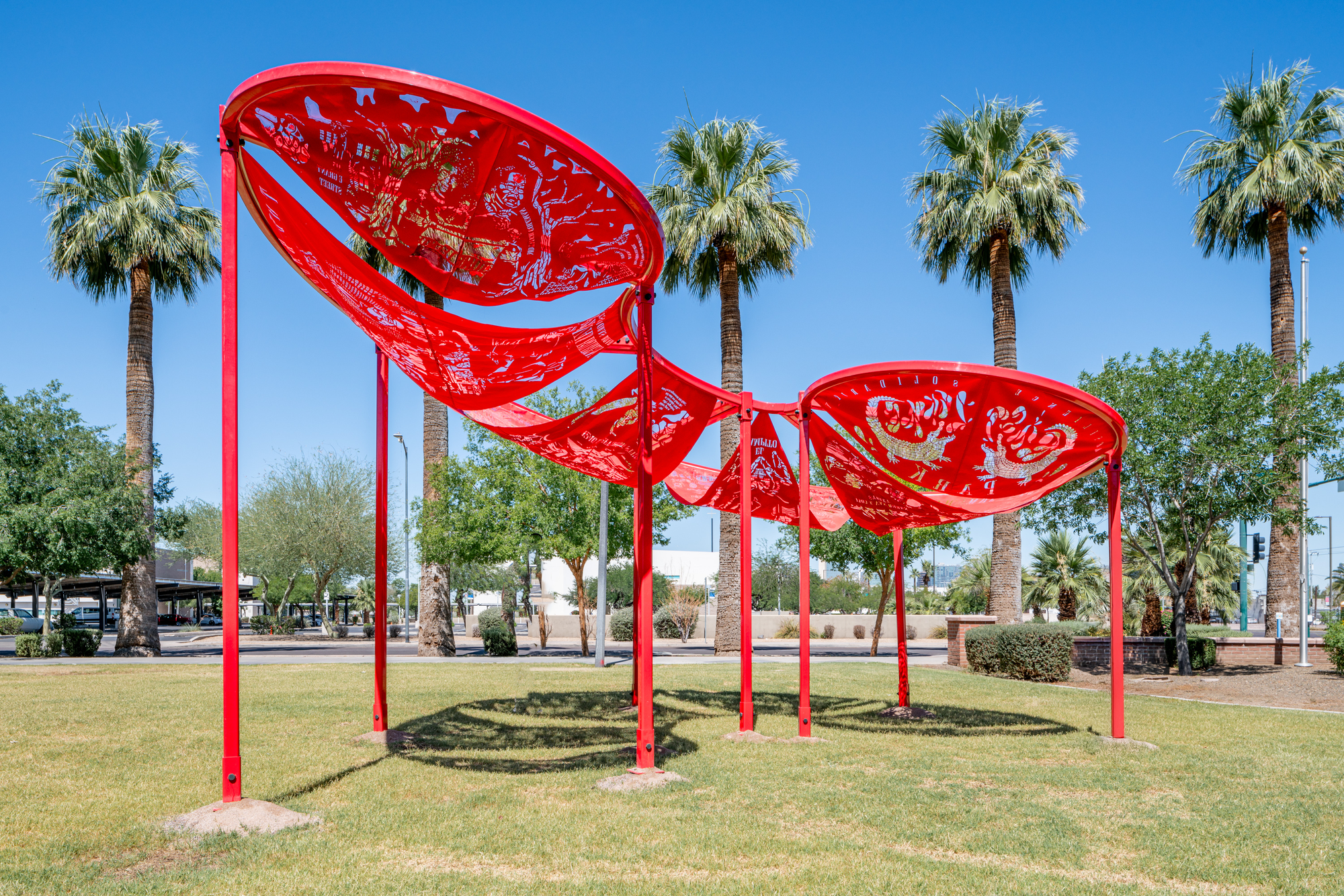 A vibrant red sculptural shade structure in a park, with patterned cut-outs that echo motifs used in the Chinese Chorizo Project.