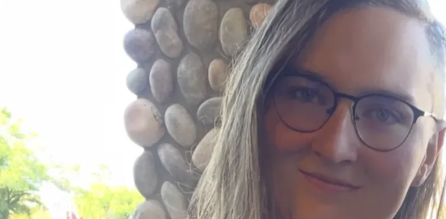 An image of a blonde woman with glasses, smiling.