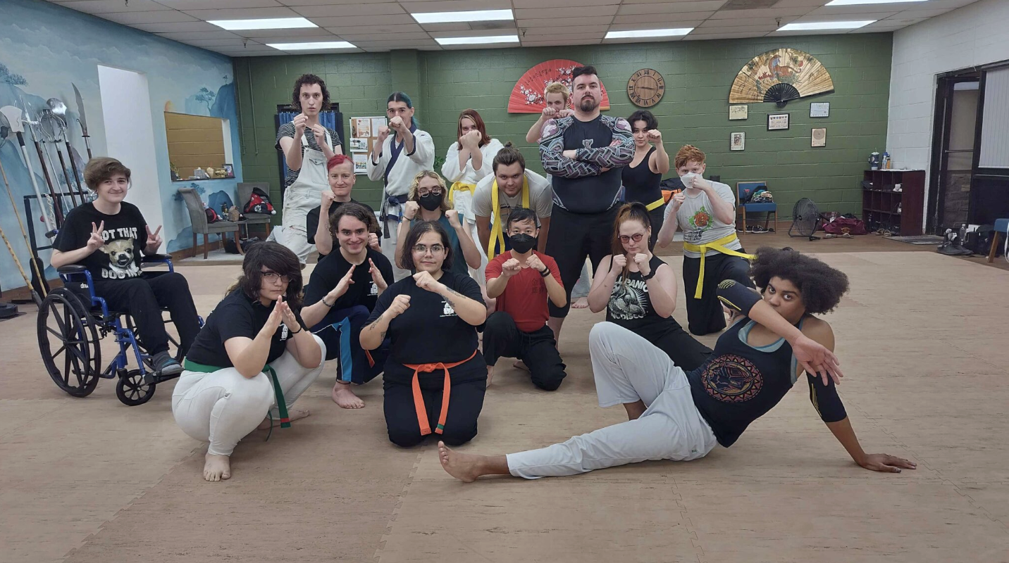 A diverse group of individuals in martial arts attire striking fighting poses, promoting LGBTQ safety and inclusivity.
