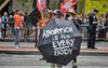 A protester walks in a street demonstration holding a black umbrella painted with the words “Abortion is for Everybody,” part of a rally responding to abortion restrictions.