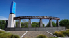 A sign for Mesa Community College with a blue pillar, trees, and a clear sky in the background.