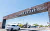 Street view of the Melrose District archway in Phoenix, Arizona, with cars driving beneath the large metal structure on a sunny day.