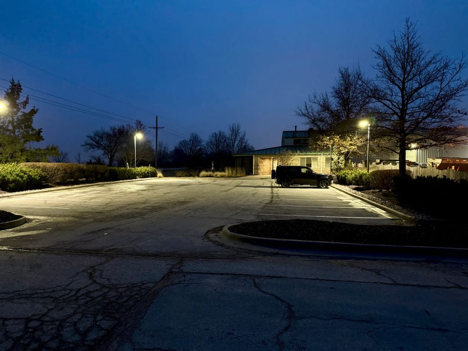 A single black SUV parked alone under streetlights in an empty office parking lot at dusk.
