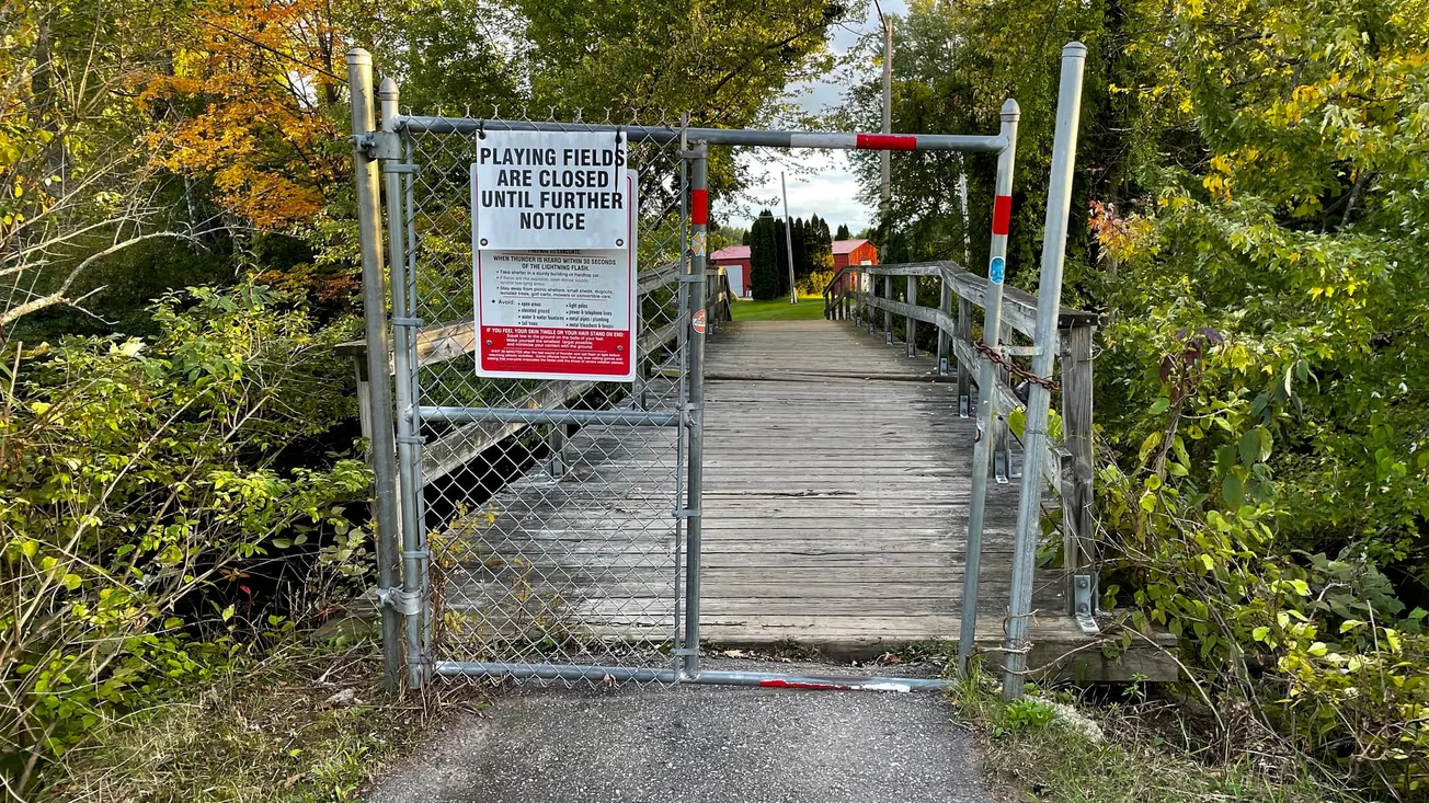 Photo by Frederick Lane in 2021 of a fence gate with a hole on one side, in Keene, New Hampshire
