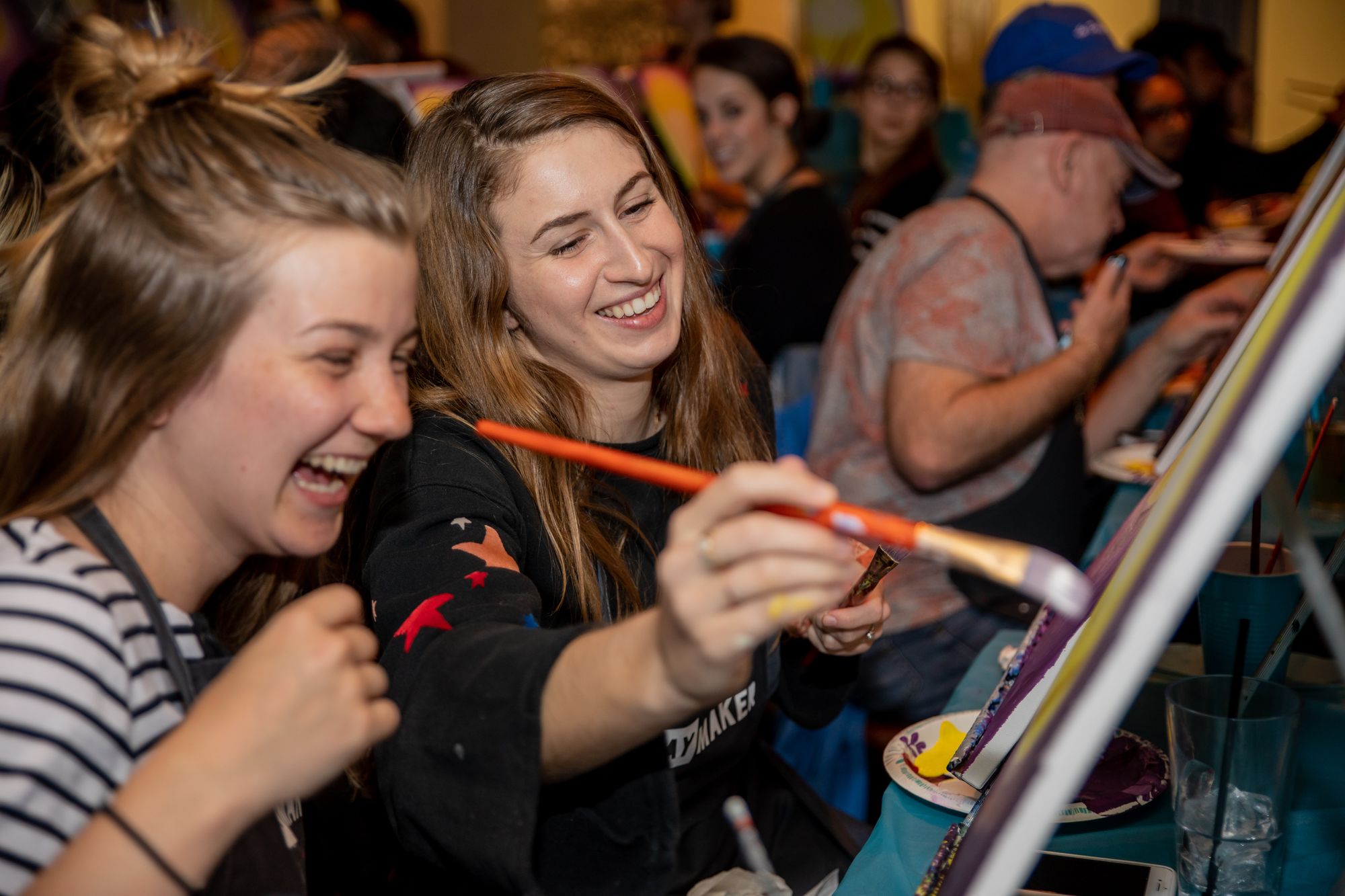 Young women laughing at a Paint Nite paint and sip party.