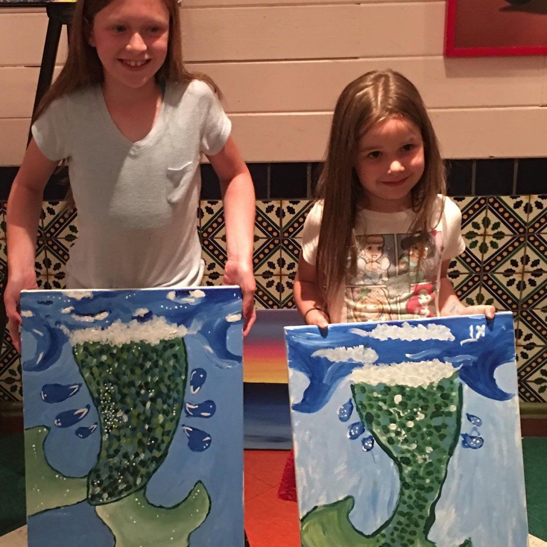 Sisters holding up fished paintings from a family paint night