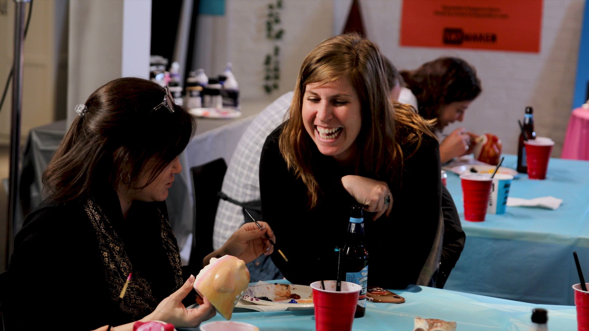 Paint Nite host laughing with guest at ceramics event.