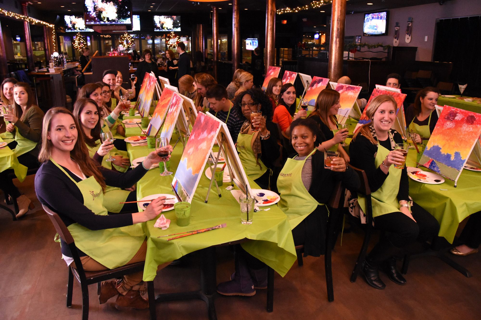 Group smiling and cheersing at a paint and sip party with PaintNite.com