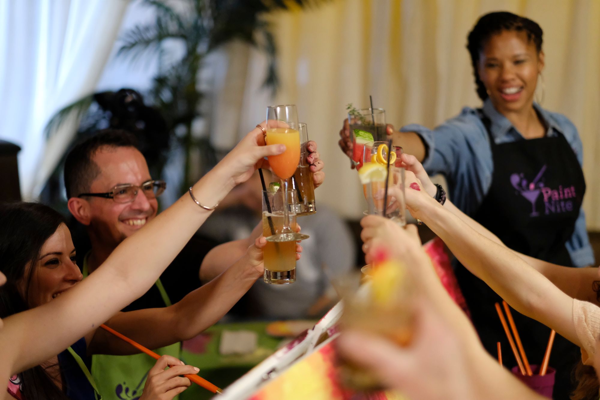 Group cheersing with a Paint Nite host at a sip and paint party.