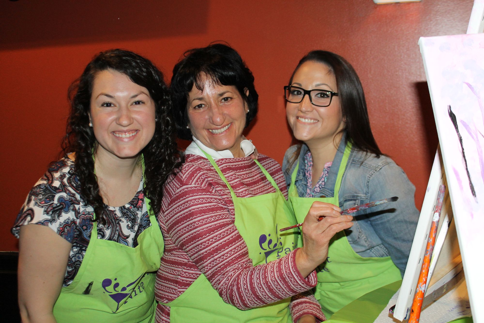 Mom and two daughters smiling while painting at Mother's Day event