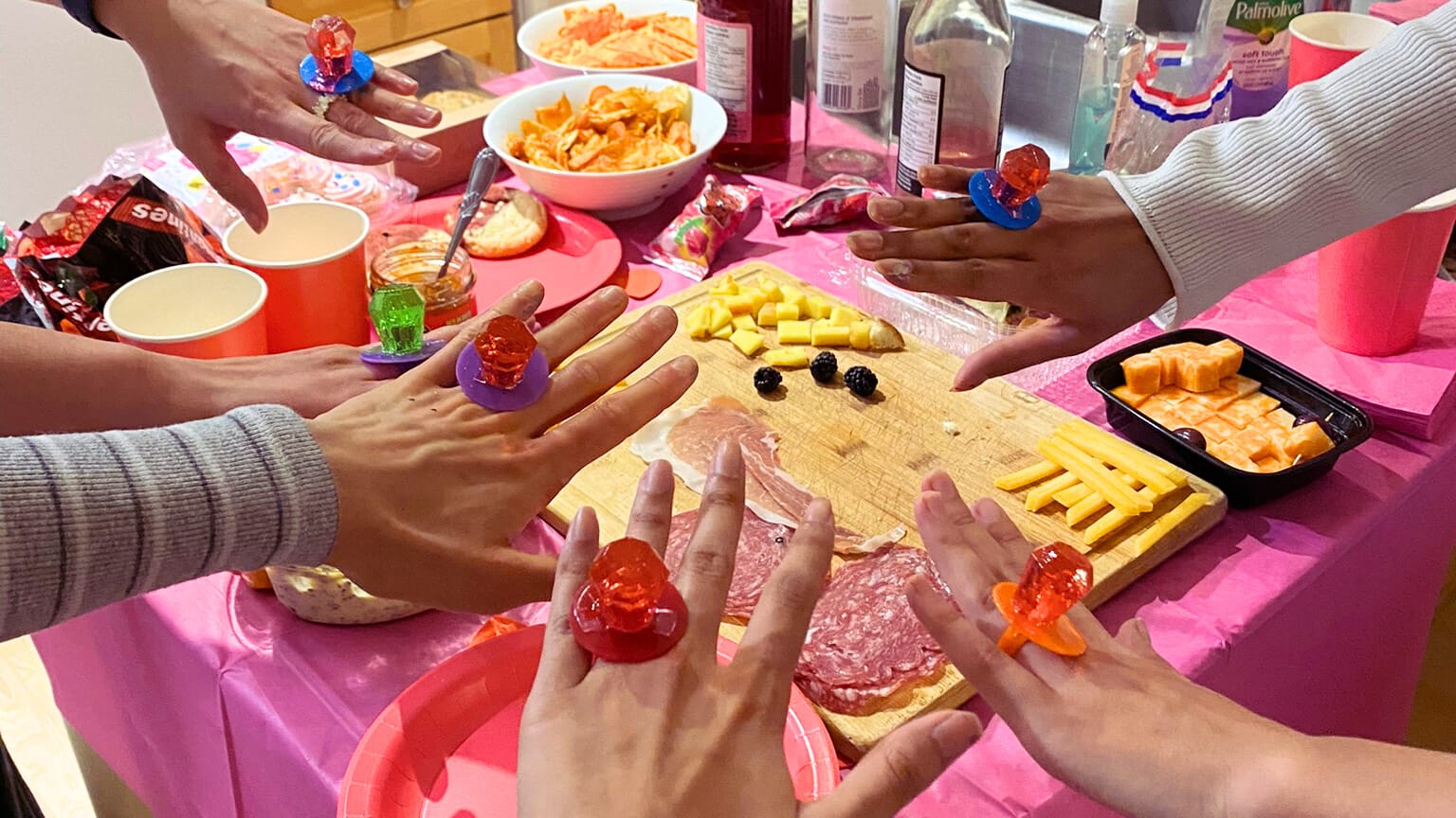 Food buffet on pink tablecloth and girls hands with candy ring