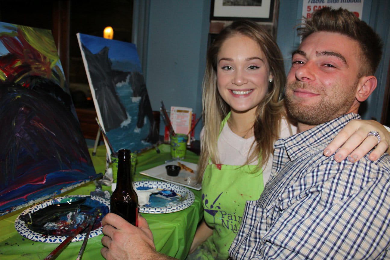 Couple showing off completed paintings after paint and sip event at local restaurant, holding colorful artwork