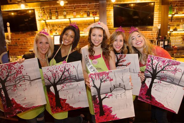 Bachelorette party group holding painted canvases at paint and sip event