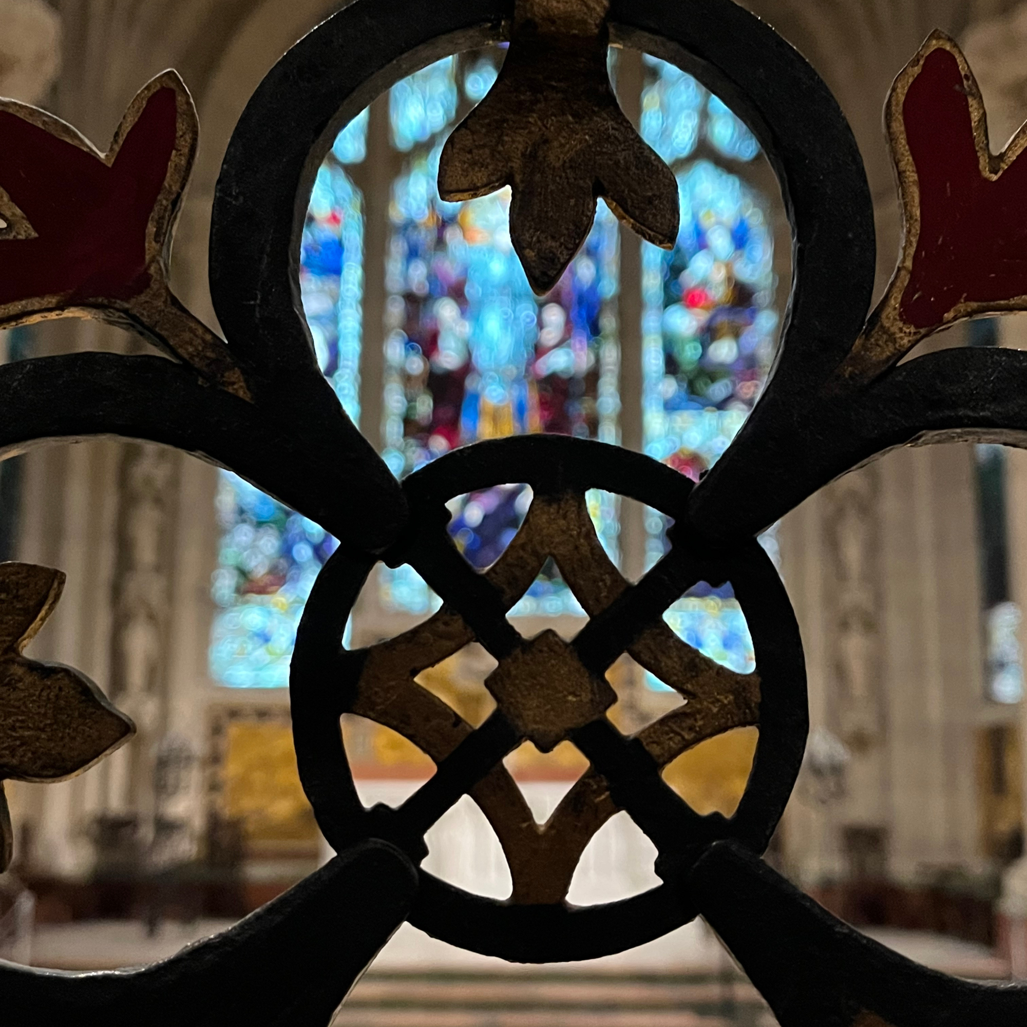 close up photo of black ironwork in the foreground and stained glass in the background in a church chapel 