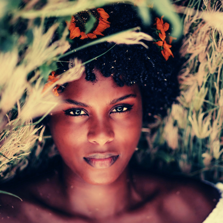 photo of a black woman lying in grass with wildflowers in her hair