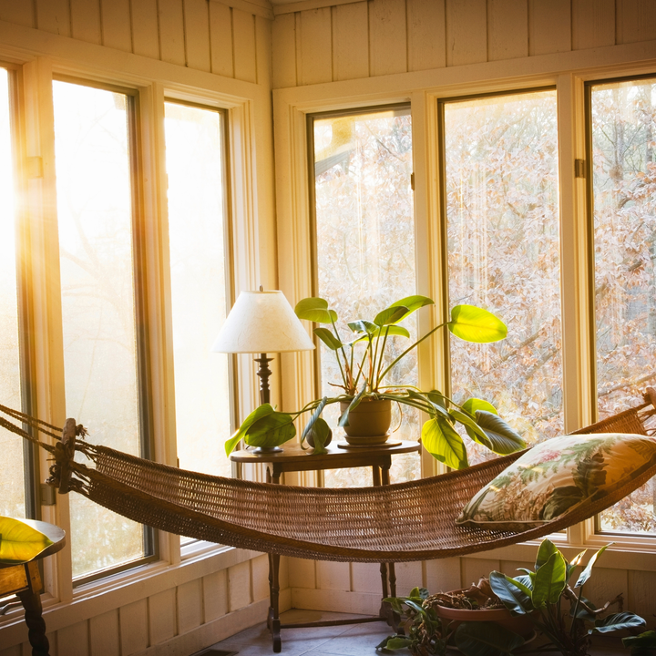 photo of sunroom with a wicker hammock and tall windows in the background