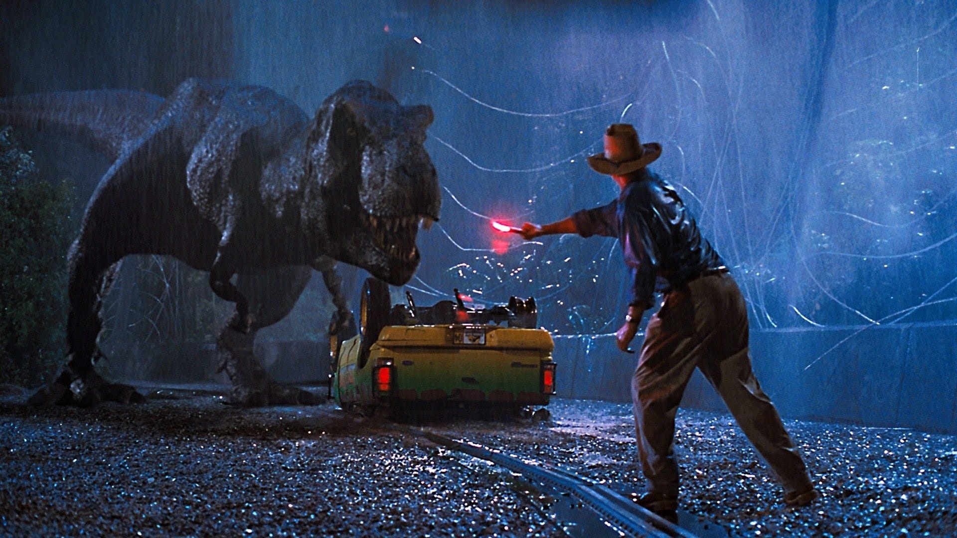 A dramatic shot from Jurassic Park shows a t-red in the rain and a man holding a flare to distract it