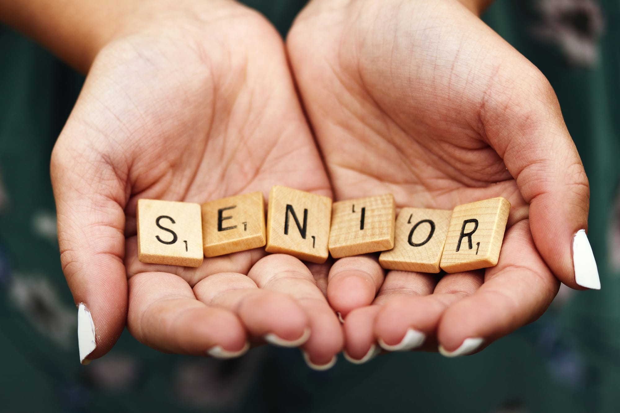 Mâini care țin litere din lemn formând cuvântul Senior