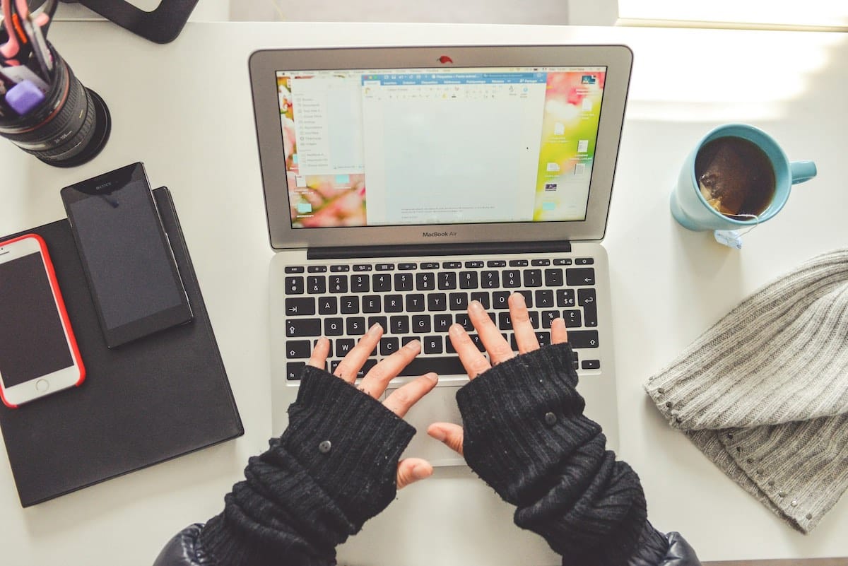 Donna seduta che usa lo smartphone davanti al laptop, in un contesto professionale e ordinato