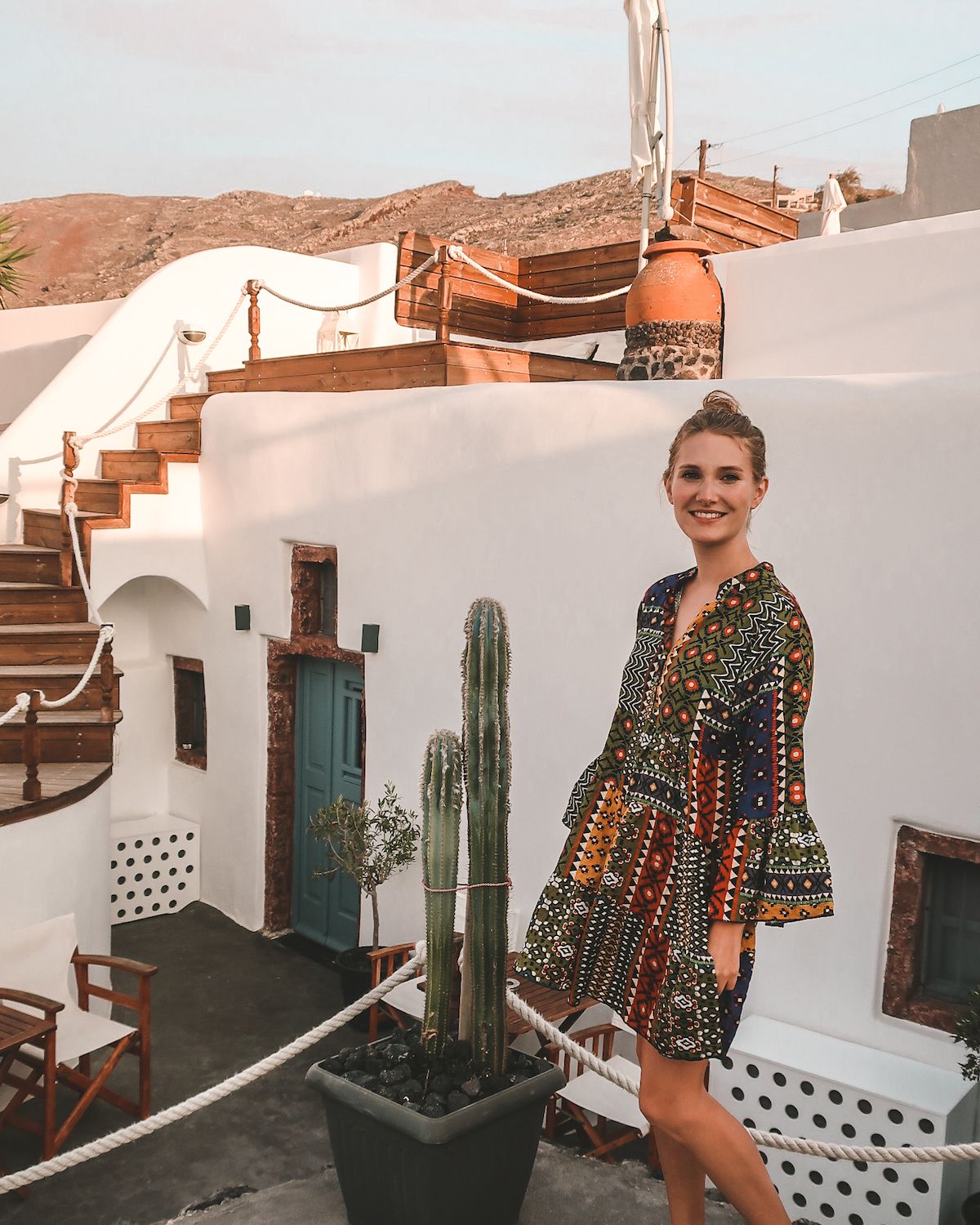 Cec, with blonde hair and blue eyes, standing outside in a colourful dress on Santorini