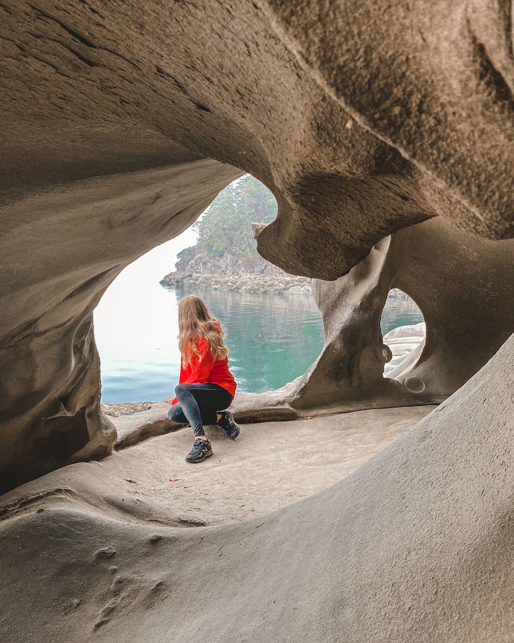 Cecily gazing through the natural rock openings of a sandstone cave on Galiano Island.