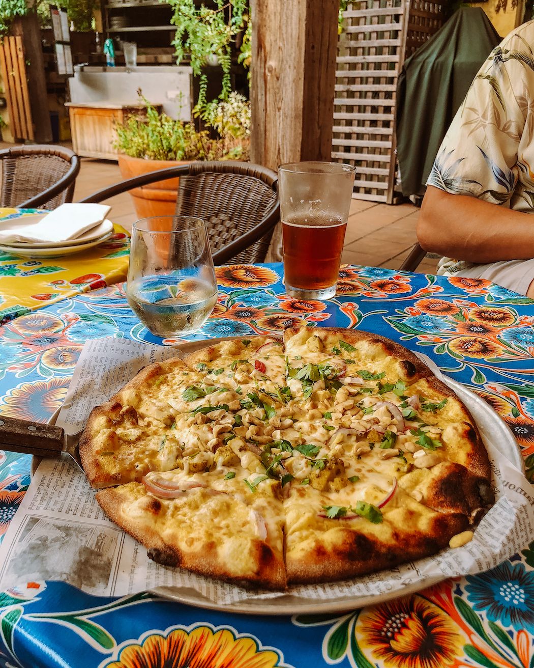 Fresh wood-fired pizza served at a cafe patio with a colourful island vibe.