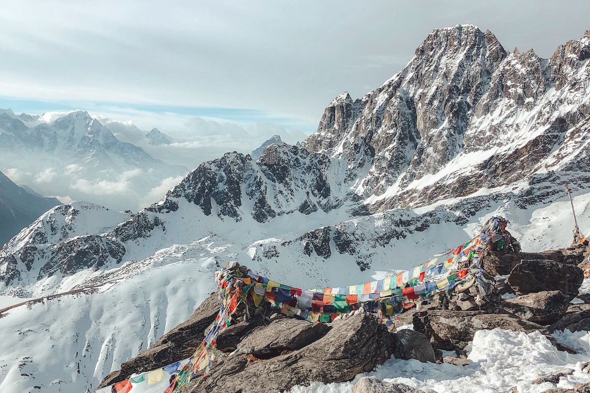 Snowy Himalayan peaks with colourful prayer flags strung between rocks in the foreground on the Gokyo Ri summit in Nepal.